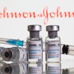 Vials labelled “COVID-19 Coronavirus Vaccine” and sryinge are seen in front of displayed J&J logo in this illustration