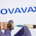 FILE PHOTO: A woman holds a small bottle labeled with a “Coronavirus COVID-19 Vaccine” sticker and a medical syringe in front of displayed Novavax logo in this illustration