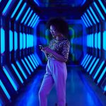 Young businesswoman looking at smartphone in spaceship like corridor