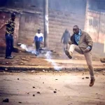 Kenyan protester kicking away tear gas